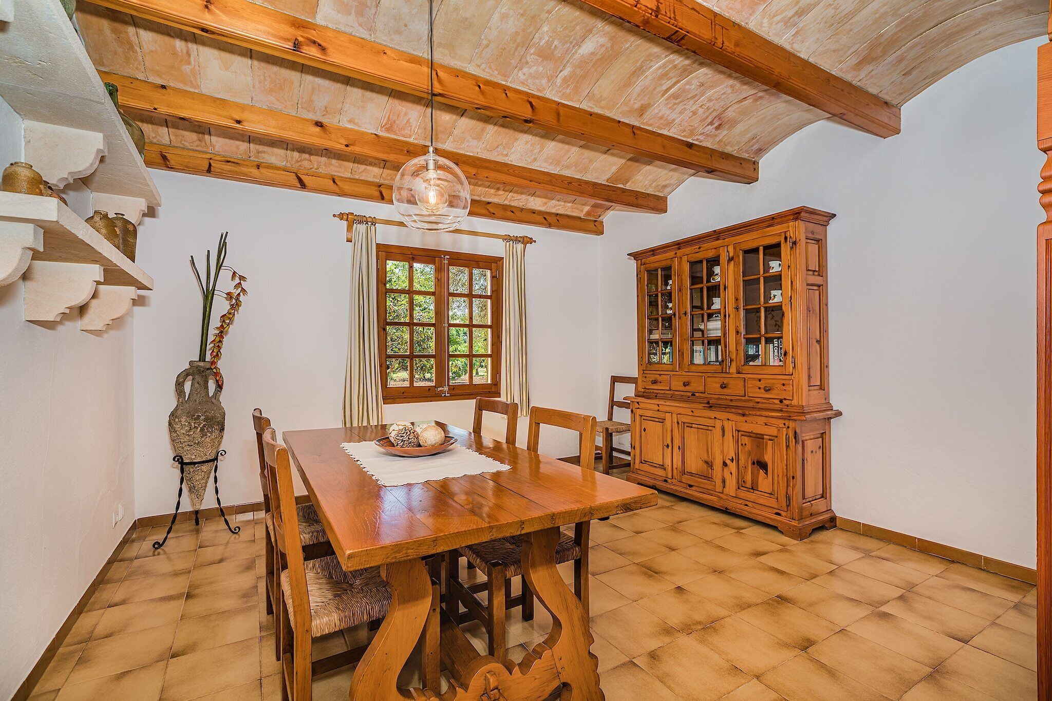 A dining room with a wooden table and chairs, a cabinet with glass doors, and a window with curtains.