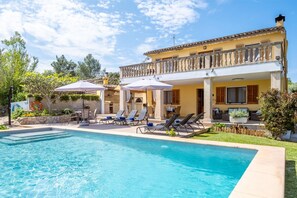 Ein Poolbereich mit Liegestühlen und Sonnenschirmen, ein klares, blaues Schwimmbecken und ein Gebäude mit Balkonen.
