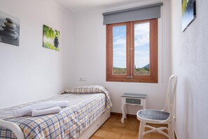 Ein kleines Schlafzimmer mit einem Bett, einem Sessel, einem Nachttisch und einem Fenster mit Blick ins Freie.