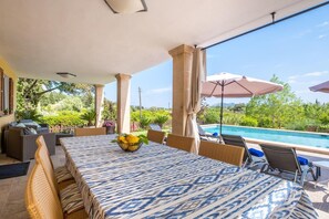Un patio exterior con piscina, zona de estar techada y mesa con mantel estampado.