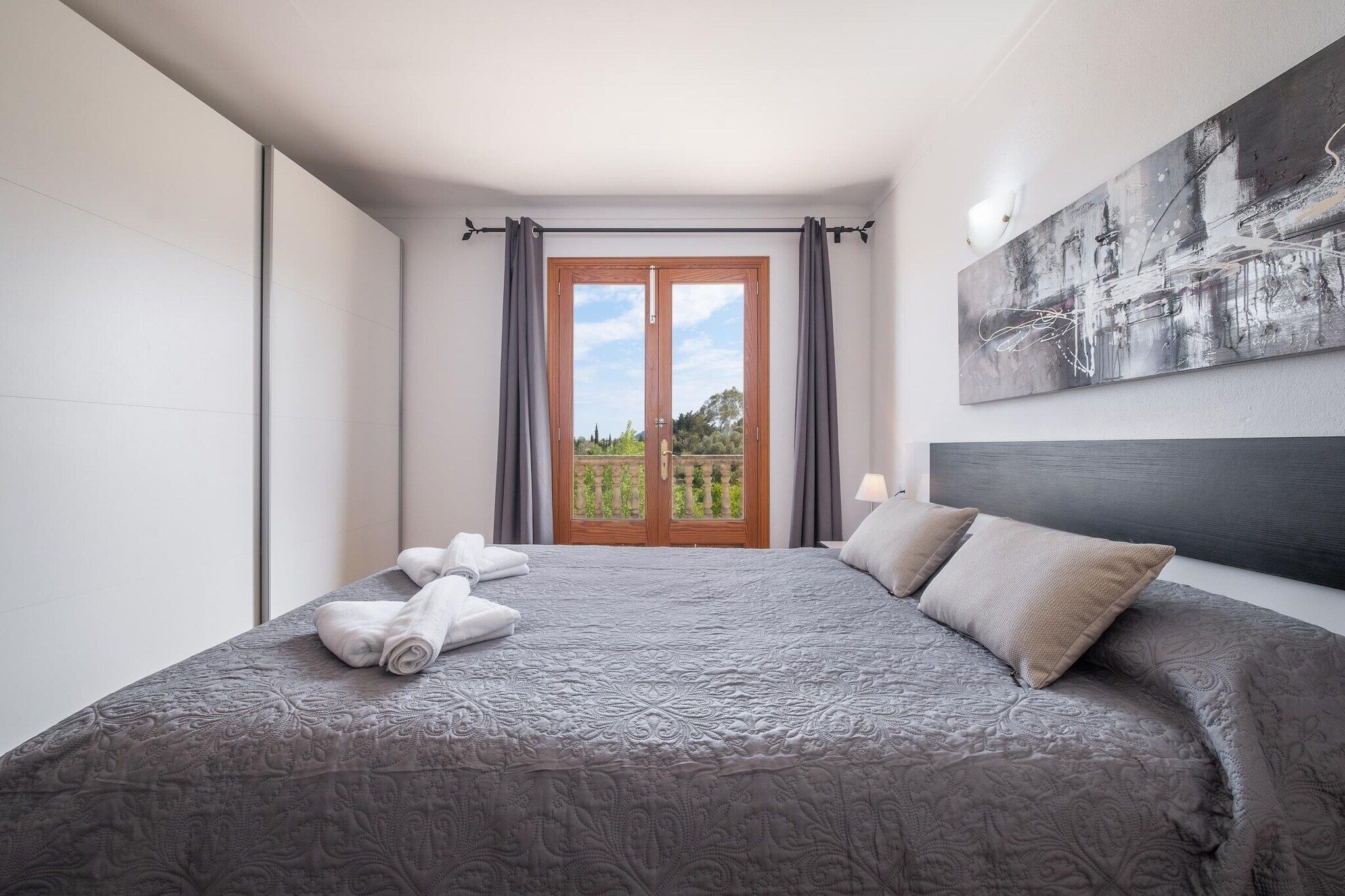 A hotel room with a large bed, a view of the outdoors through a glass door, and a modern abstract painting on the wall.