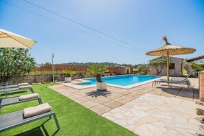 Ein Garten mit Swimmingpool, Sonnenschirm und Liegestühlen.