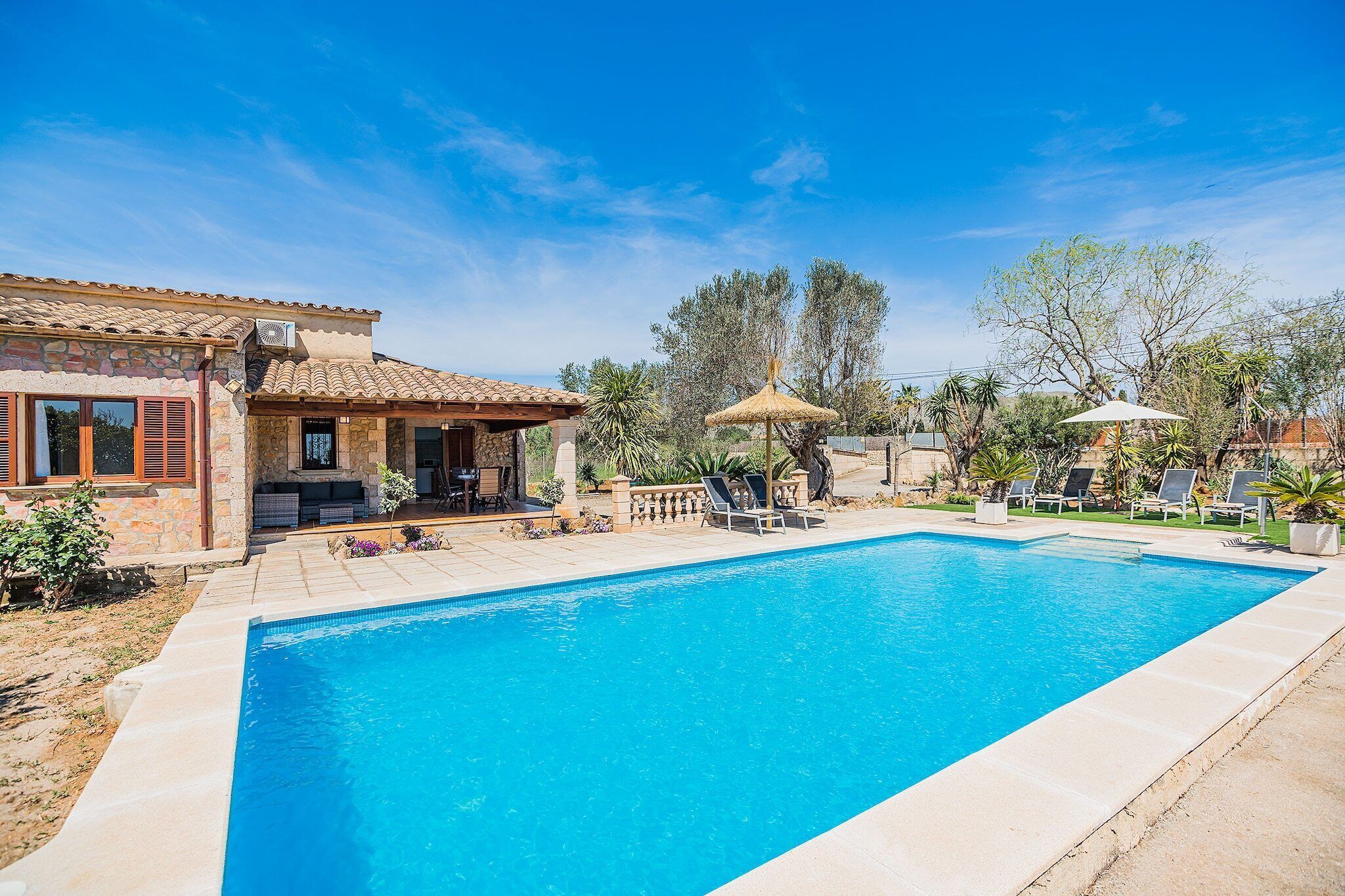 A swimming pool with a patio area, a covered seating area, and a stone building with a tiled roof.
