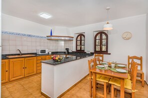 Eine Küche mit Holzschränken, einer Mikrowelle, einer Kaffeemaschine und einem Essbereich mit Tisch und Stühlen.