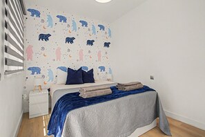 Ein Schlafzimmer mit einem Bett, Kissen, einem Nachttisch und einer Wand mit Bären- und Sterndruck.