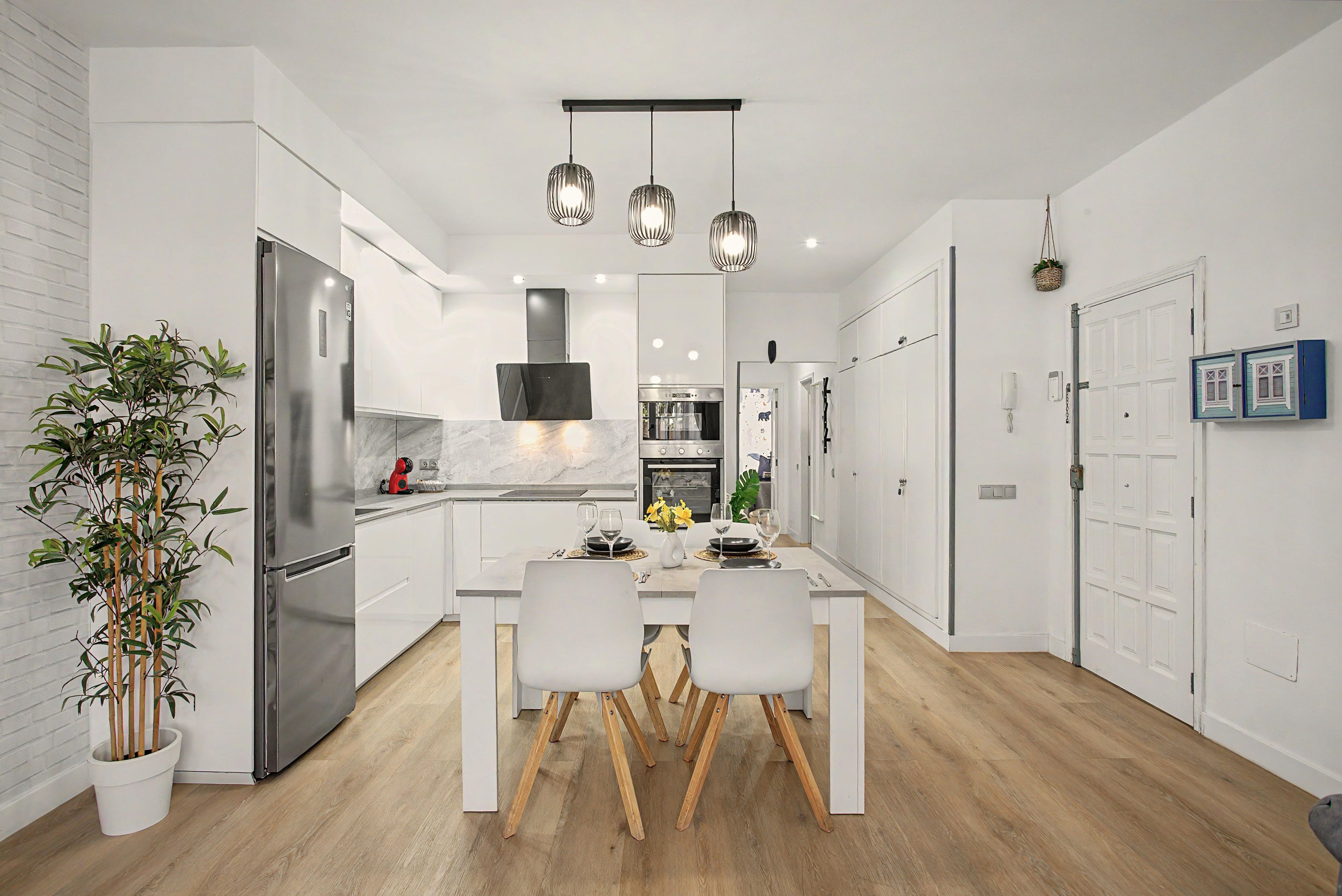 A modern kitchen with white cabinetry, a stainless steel refrigerator, and a dining area with a white table and chairs.