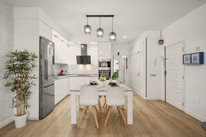 Eine moderne Küche mit weißen Schränken, einem Edelstahlkühlschrank und einem Essbereich mit weißem Tisch und Stühlen.