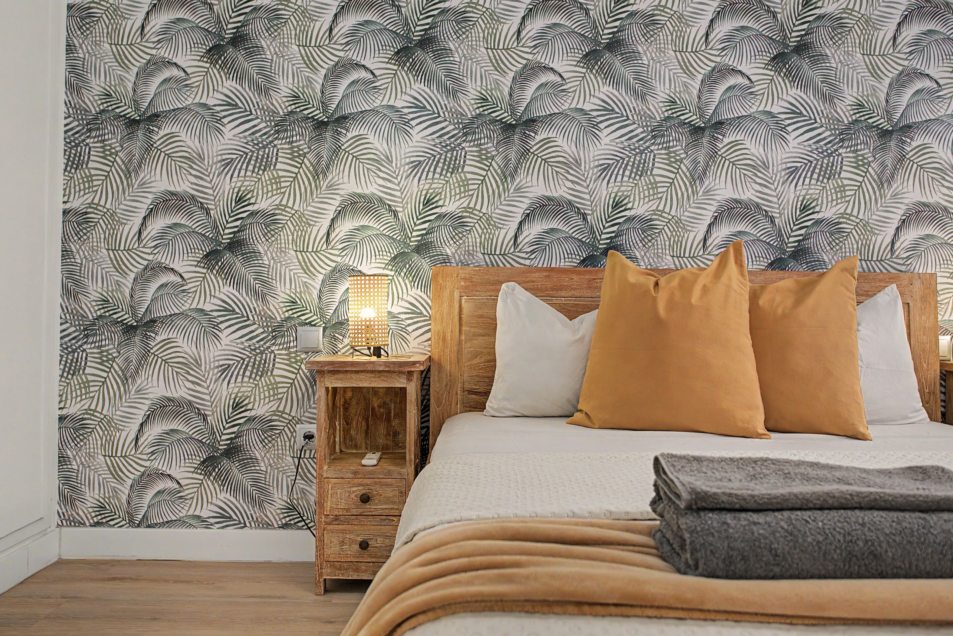 Een slaapkamer met een bed, kussens, een nachtkastje en een wand met een bladmotief.