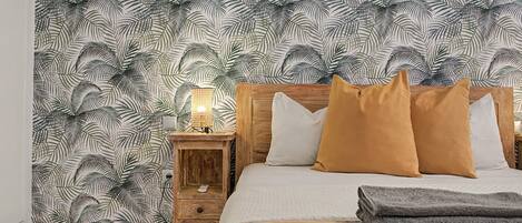Une chambre à coucher avec un lit, des oreillers, une table de chevet et un mur orné d’un motif de feuilles.