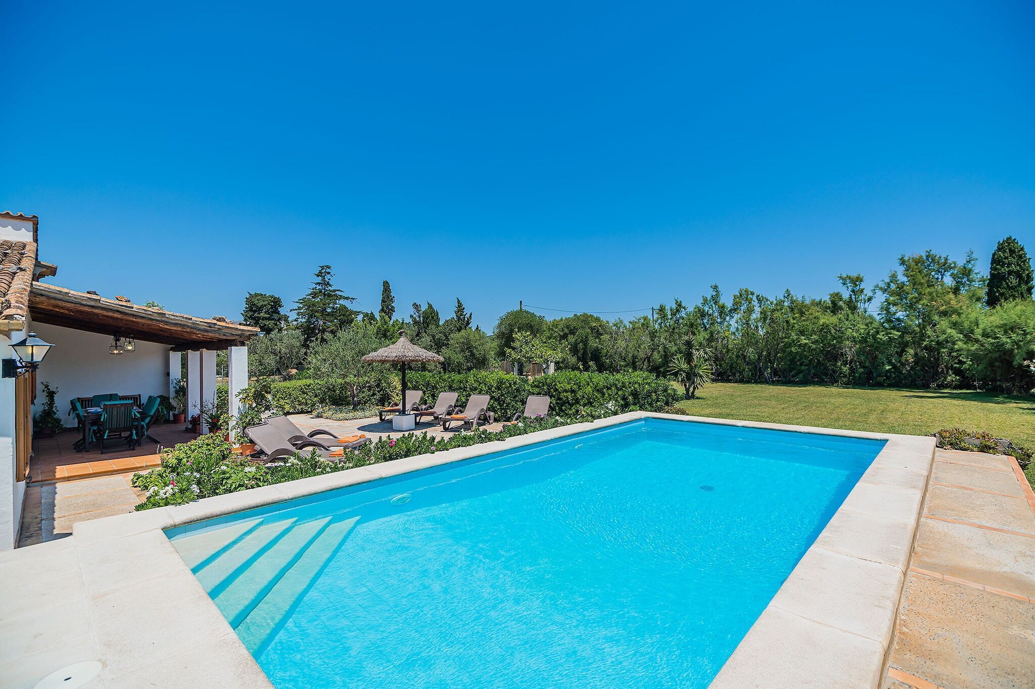 A rectangular swimming pool with a clear blue surface, surrounded by a paved deck.
