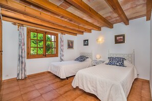 Un dormitorio con dos camas, vigas de madera en el techo, una ventana con vistas a la vegetación y una lámpara fijada a la pared.