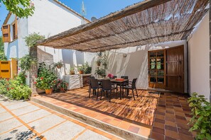 Un patio cubierto con una mesa y sillas, rodeado de plantas en macetas y un suelo de baldosas.