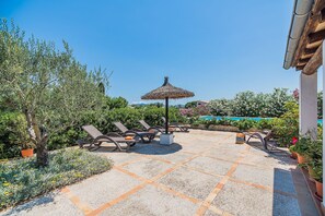 A patio with sun loungers, a thatched umbrella, and potted plants. - Secluded Country Villa with Pool (Pollensa / Pollença)