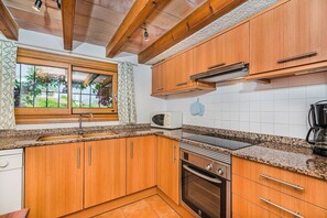 A kitchen with wooden cabinets, a built-in microwave, a stove, and a window with a view of greenery. - Secluded Country Villa with Pool (Pollensa / Pollença)