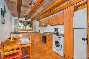 A compact kitchen with wooden cabinets, a built-in oven, a washing machine, and a dining area with a table and chairs. - Secluded Country Villa with Pool (Pollensa / Pollença)