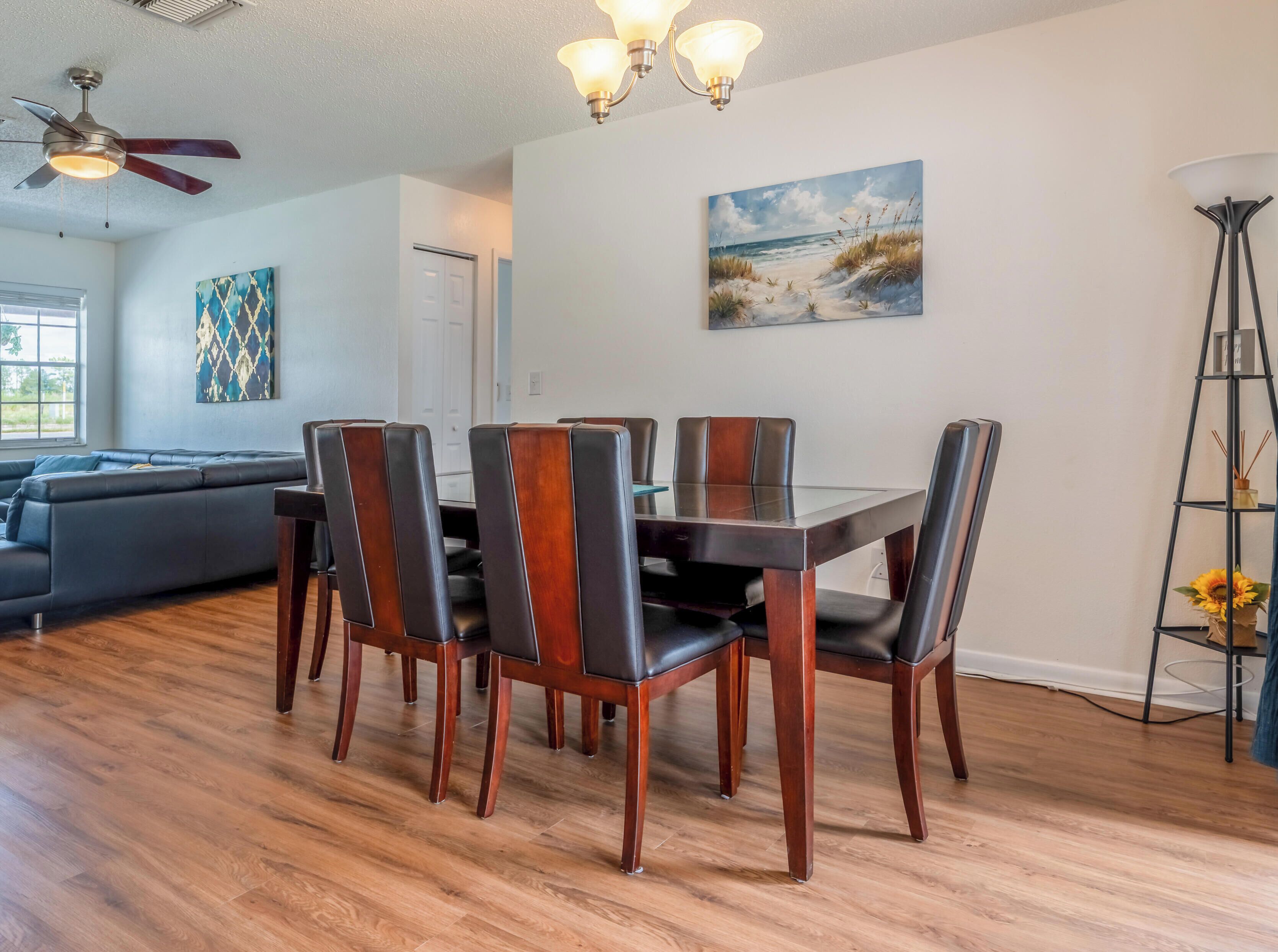 A dining area with a wooden table and chairs, a ceiling fan, a painting, and a floor lamp.
