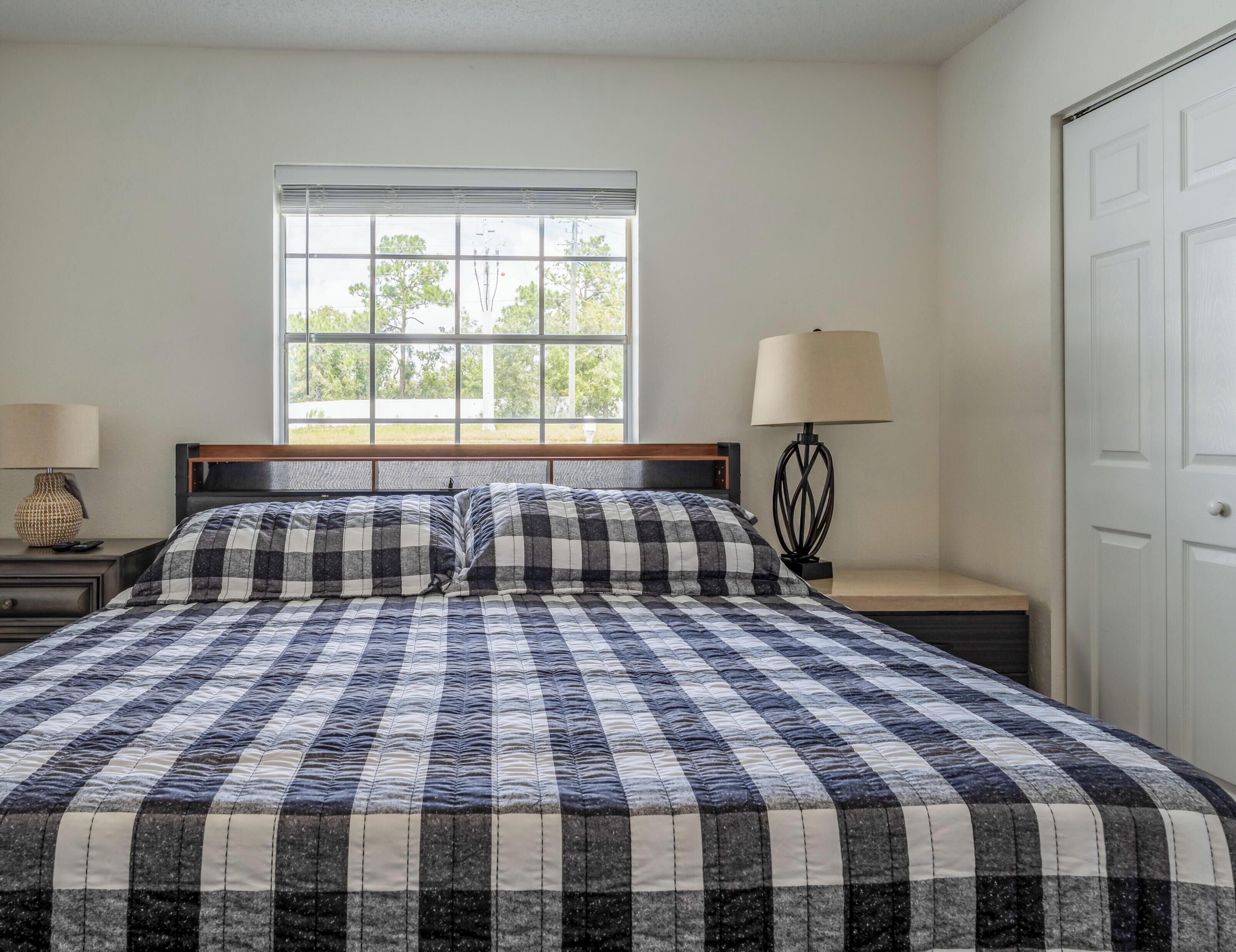 A bedroom with a large bed, a window, a nightstand with a lamp, and a door.