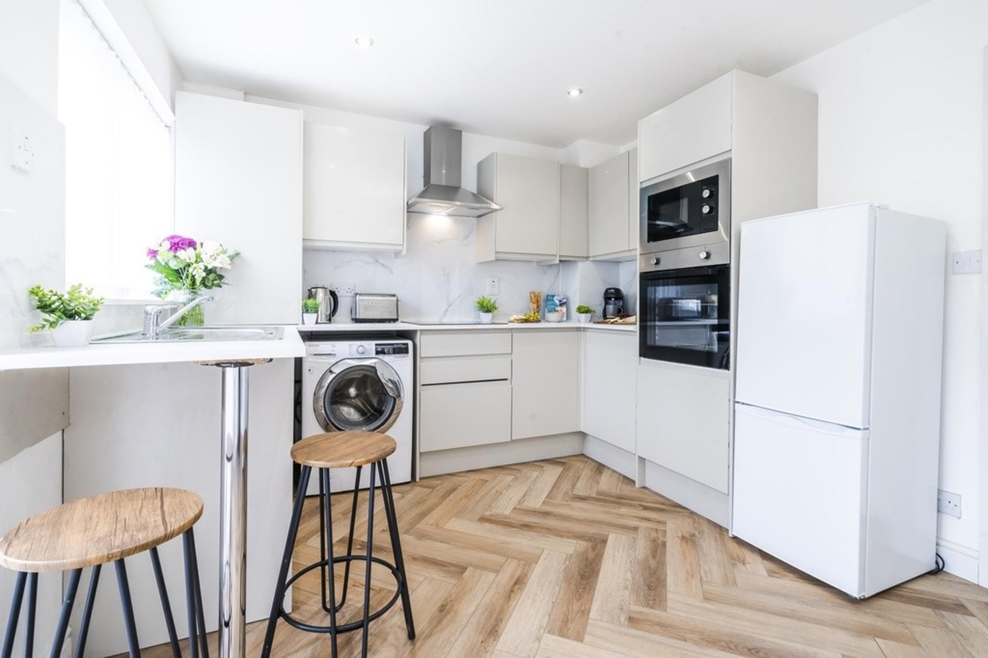 Eine moderne Küche mit weißen Schränken, einer integrierten Waschmaschine, einer Kaffeemaschine und einem Kühlschrank.