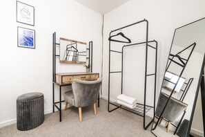 A room with a wooden desk, a grey chair, a hanging clothes rack, a large mirror, and a small stool. - 3br 1 Bath Sleeps 7 Parking (Oldbury)