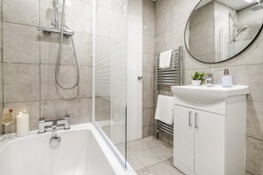 Ein modernes Badezimmer mit einer gläsernen Duschkabine, einem weißen Waschtisch und einem runden Spiegel.