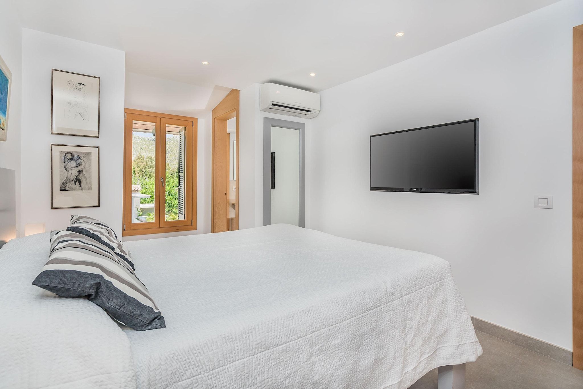 Un dormitorio con cama, televisor y puerta que da a un balcón.