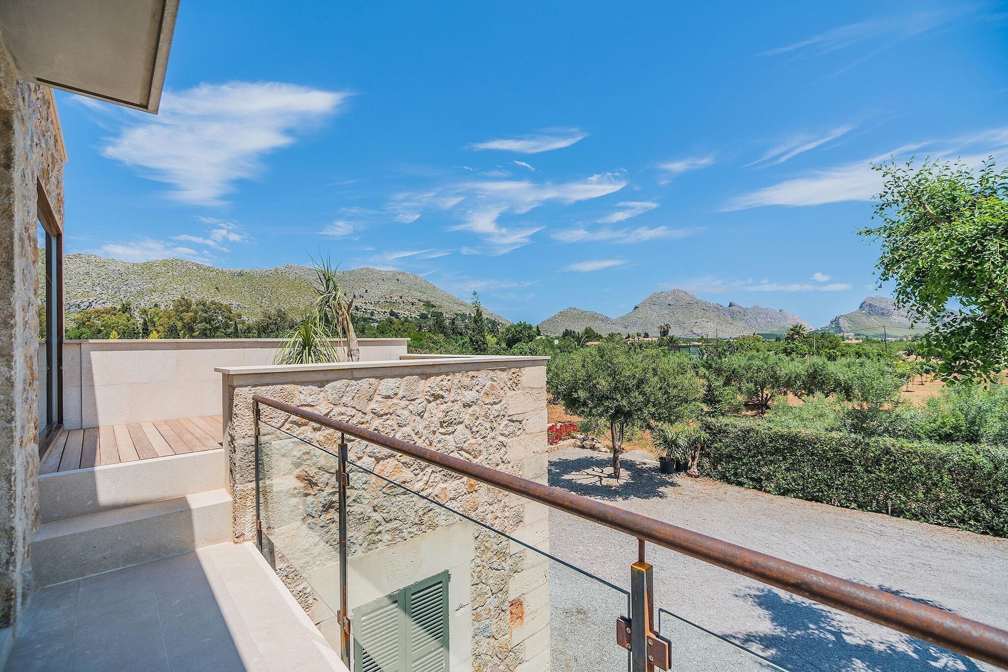 A balcony with a view of a mountainous landscape, a stone wall, and a metal railing.