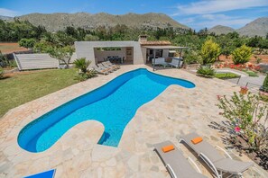 Ein Pool mit ungewöhnlicher Form, umgeben von einer Steinterrasse und Gartenmöbeln.