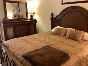 A bedroom with a wooden bed, a nightstand, a lamp, and a mirror. - Lovely 2 bedroom and den house sleeping 6. Quiet with many great amenities. (North Fort Myers)