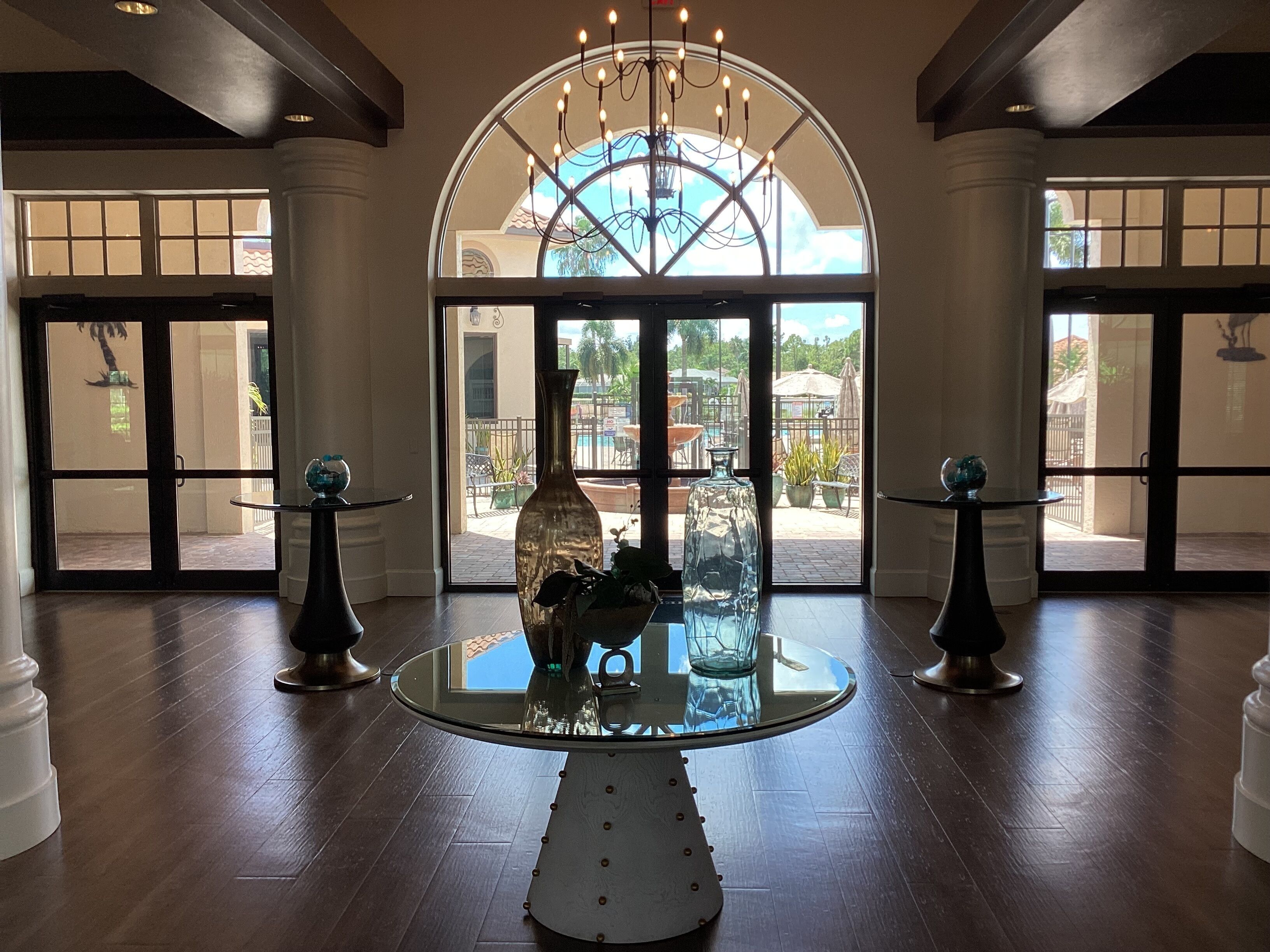 A lobby with a glass-top table, two side tables, and a large arched window with a view of the outdoor area.