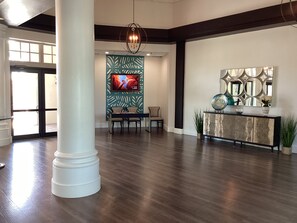 A spacious lobby with a large white column, a modern chandelier, a seating area with a table and chairs, and a decorative console with plants. - Lovely 2 bedroom and den house sleeping 6. Quiet with many great amenities. (North Fort Myers)