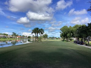 Un campo de golf con un estanque, árboles y casas al fondo.