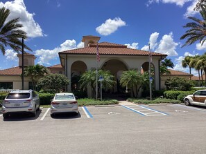 A building with a tiled roof, multiple arches, and a flagpole. There are parking spaces with blue lines and a handicap sign. - Lovely 2 bedroom and den house sleeping 6. Quiet with many great amenities. (North Fort Myers)