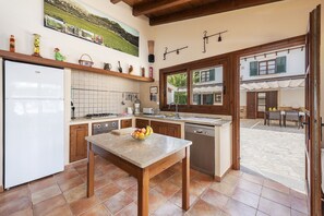 A kitchen with a refrigerator, stove, sink, and a dining table with fruit. - Grand Majorcan Retreat with Pool (Pollensa / Pollença)