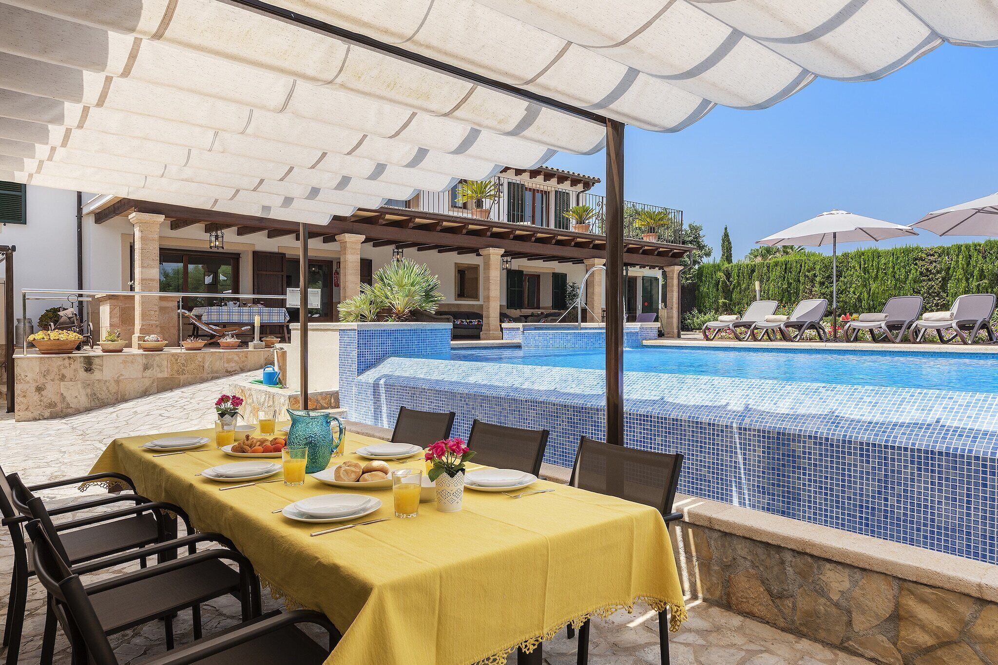 Un espace extérieur aménagé pour les repas, avec une piscine en arrière-plan.