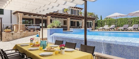 Un espacio de comedor al aire libre con una piscina al fondo.
