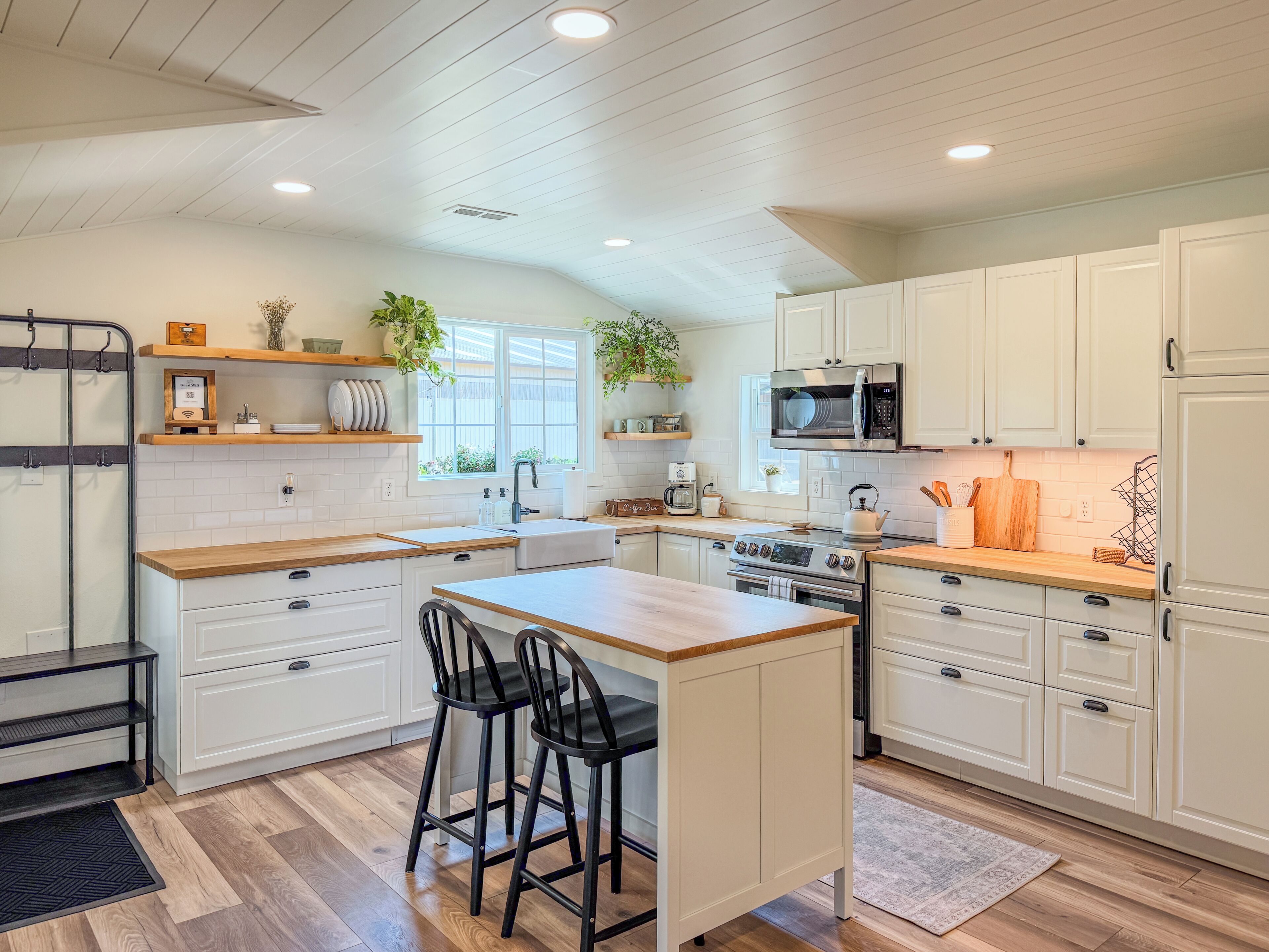 A kitchen with white cabinetry, a central island with bar stools, a microwave, and a stove.