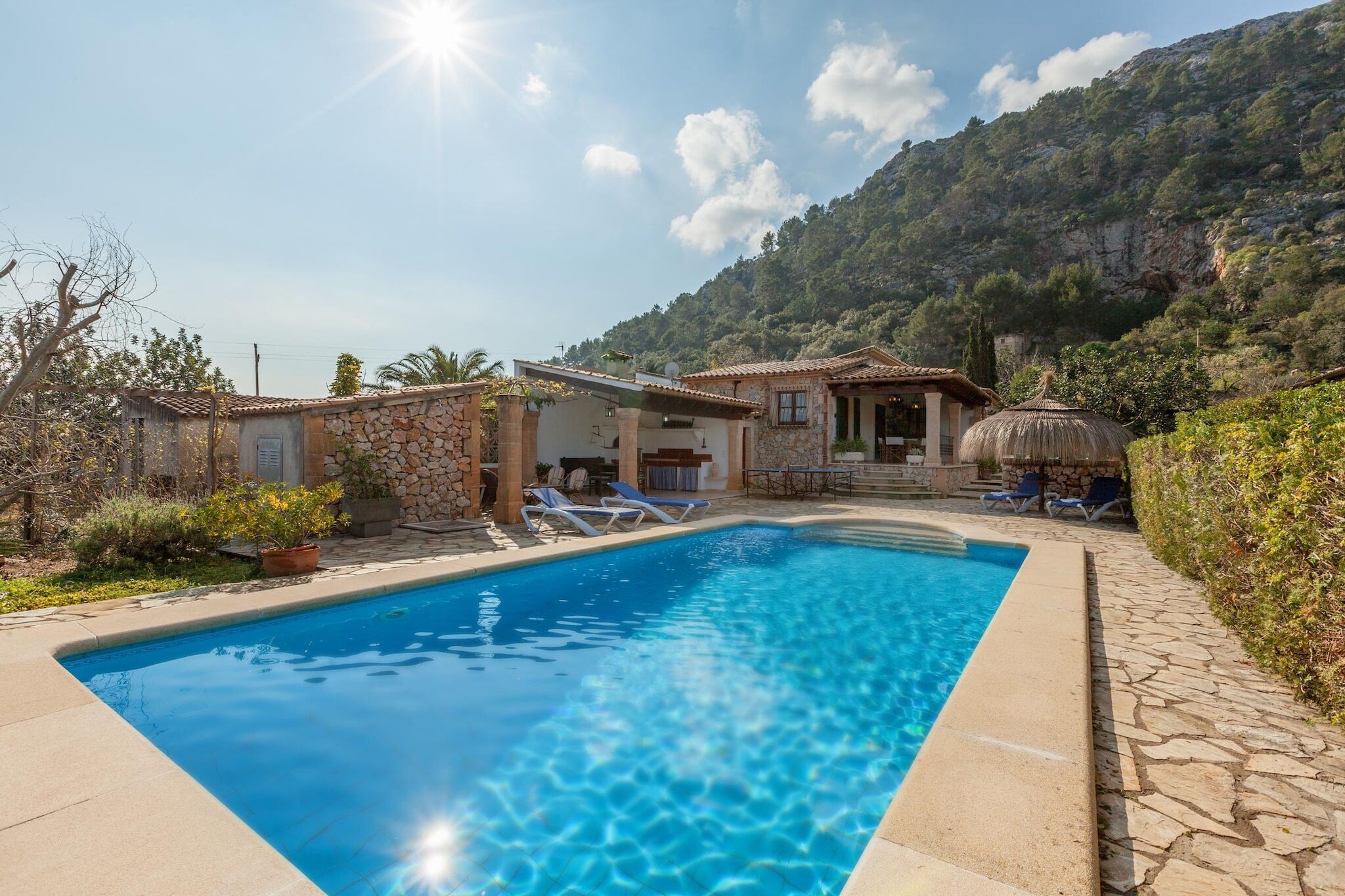 Une piscine avec des chaises longues, un bâtiment en pierre et une vue sur les montagnes en arrière-plan.