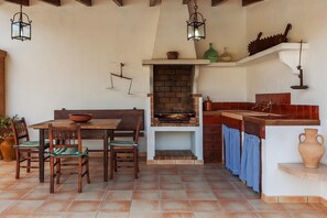 A rustic kitchen with a brick oven, wooden furniture, and hanging lanterns. - Tranquil Pollensa Villa for 5 (Pollensa / Pollença)