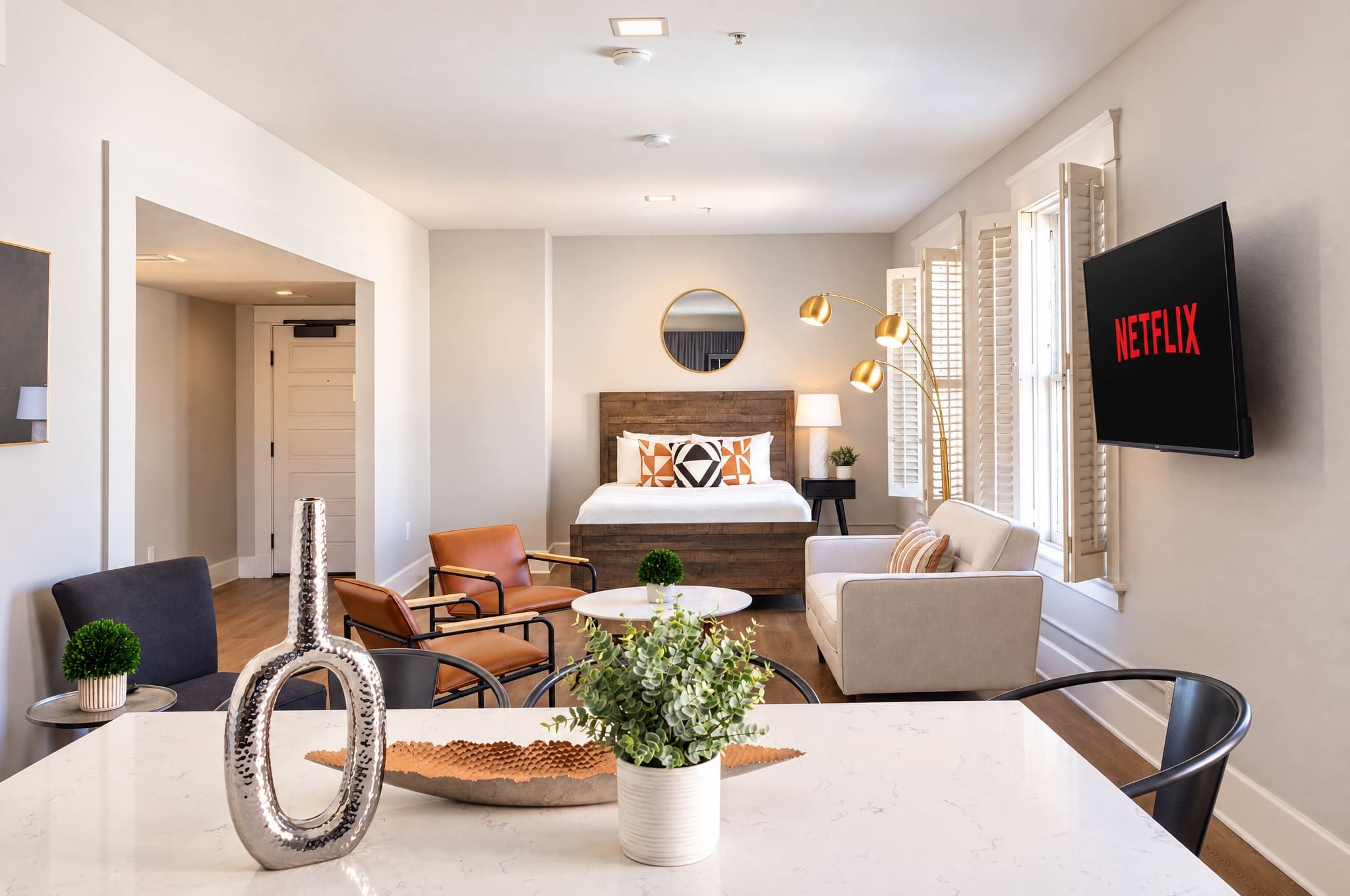 A modern hotel room with a bed, seating area, TV, and a dining table.