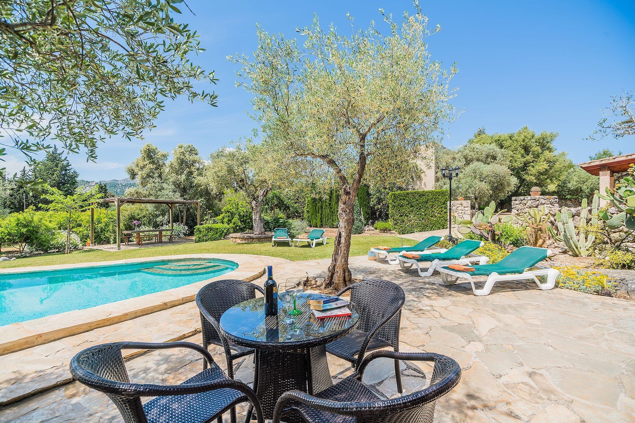 A poolside area with a table and chairs, a pool, and lounge chairs.