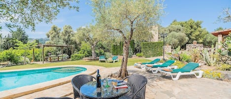 Zona junto a la piscina con mesa y sillas, piscina y sillones de descanso.
