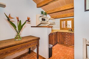 A kitchen with wooden cabinets, a microwave, and a small shelf with plants. - Rustic Country Retreat for 4 (Pollensa / Pollença)