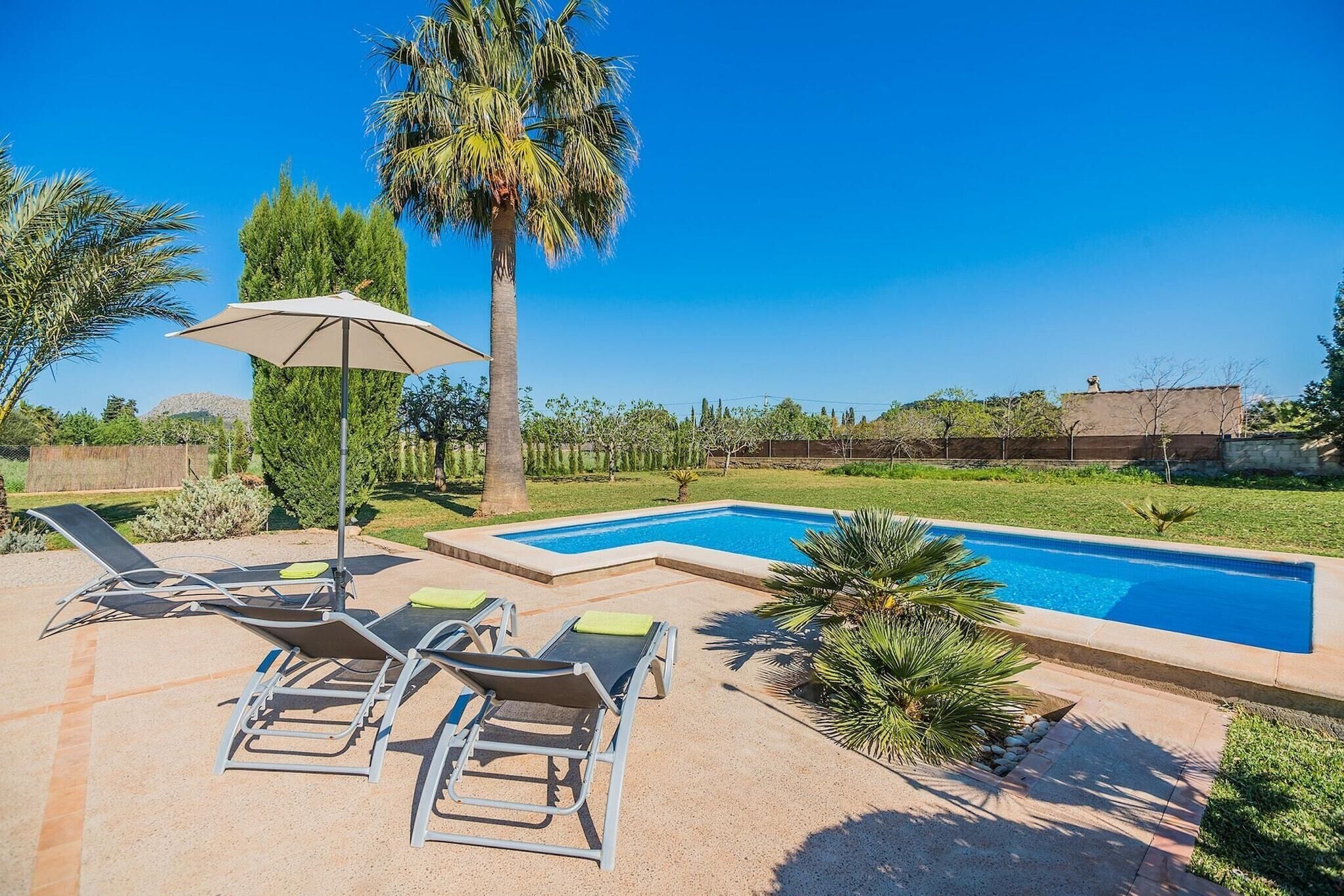 A swimming pool with lounge chairs and an umbrella, surrounded by greenery and a clear sky.