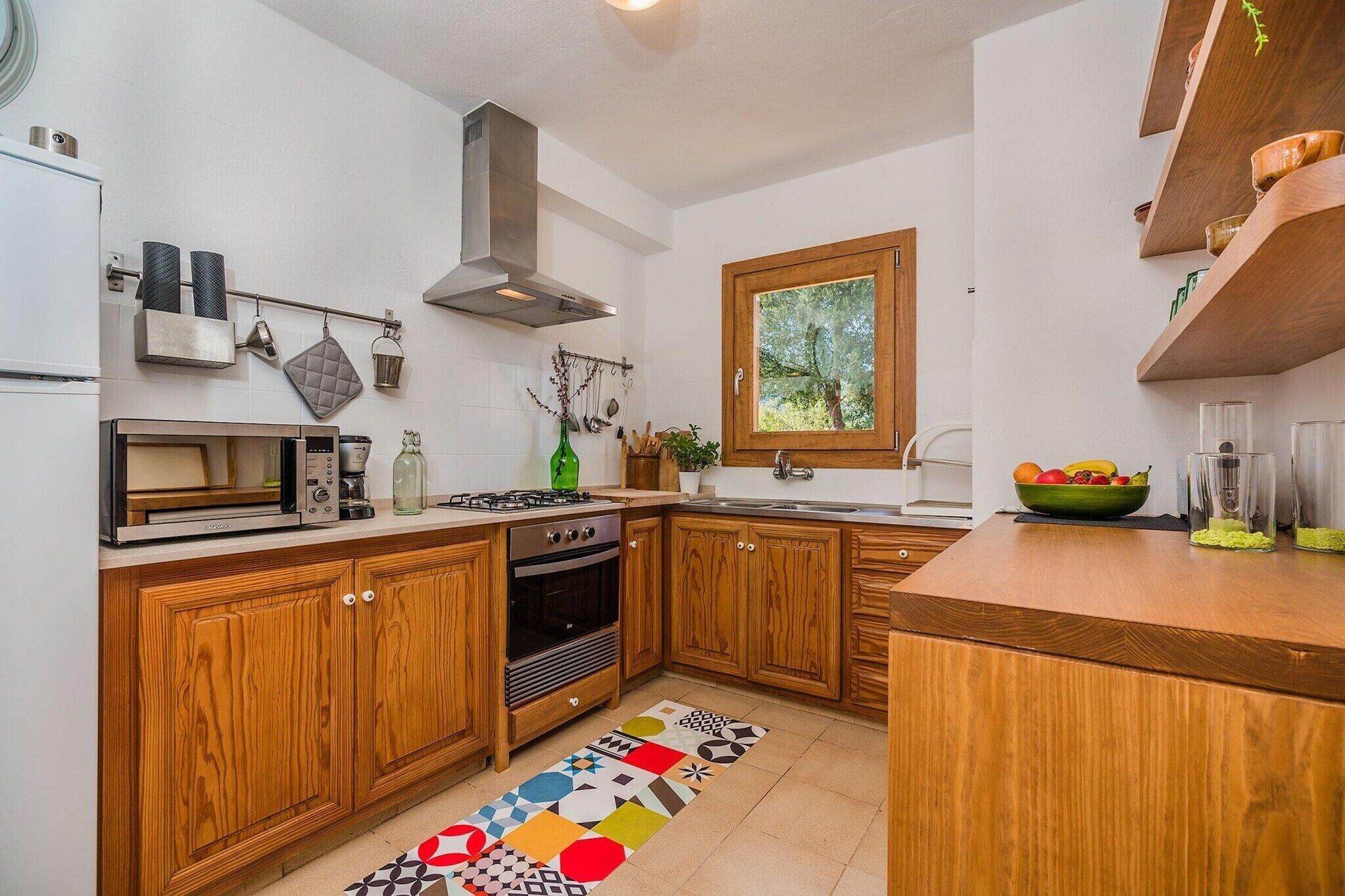 A kitchen with wooden cabinets, a gas stove, a built-in oven, a coffee maker, and a window with a view of trees.