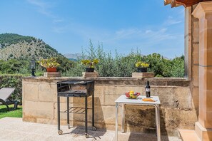 A patio with a grill, a chair, a table with a fruit bowl, and potted plants. - Single-Level Villa with Pool, Pollença (Pollensa / Pollença)