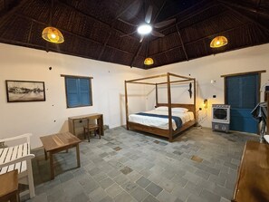 Ein Zimmer mit Himmelbett, Schreibtisch, Stuhl, Tisch und Deckenventilator.