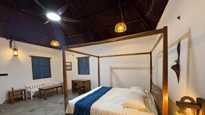 Un lit à baldaquin avec une couverture bleue, un banc en bois, une table et une lampe fixée au mur.