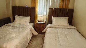 Una habitación de hotel con dos camas individuales, una mesita de noche con lámpara y una ventana con cortinas.
