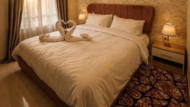Una habitación de hotel con una cama grande, una mesita de noche con una lámpara y un papel tapiz estampado.