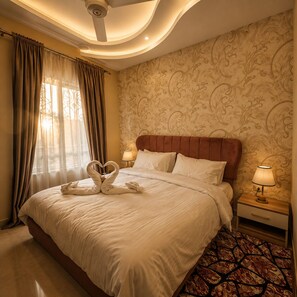 A hotel room with a large bed, a nightstand with a lamp, and a patterned wall.